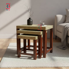 Set of three wooden nesting tables with a vase and glass on top in a living room setting.
