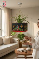 KB ART hand-painted black floral wooden hanging planter model featuring colorful vine motifs and a red bottom trim holding a green spider plant suspended by a golden chain.