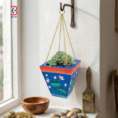 Hanging planter with floral design on a windowsill with a wooden bowl and brush.