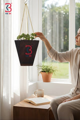 Person holding a hanging plant pot with a logo in a bright room.