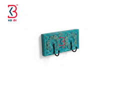 A turquoise blue carved wooden wall hook holder with three black metal hooks, shown against a plain white background with a KB Art logo in the top-left corner.