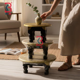 Three-tiered decorative stand with a vase on a wooden floor in a living room setting.