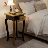 Wooden nightstand with lamp, clock, and other items next to a bed in a bedroom setting.