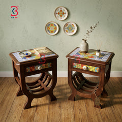 Two dark brown wooden side tables with colorful mosaic tile tops and decorative drawer fronts, styled in a room setting with a light green patterned wall, three decorative plates, and a small vase on a wooden floor.