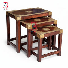 Set of three nested wooden tables with decorative patterns on a white background