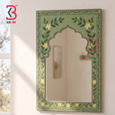 An arched decorative wall mirror with a painted green border featuring leafy vines and small yellow flowers, mounted on a light wall. A KB art logo appears in the top-left corner.