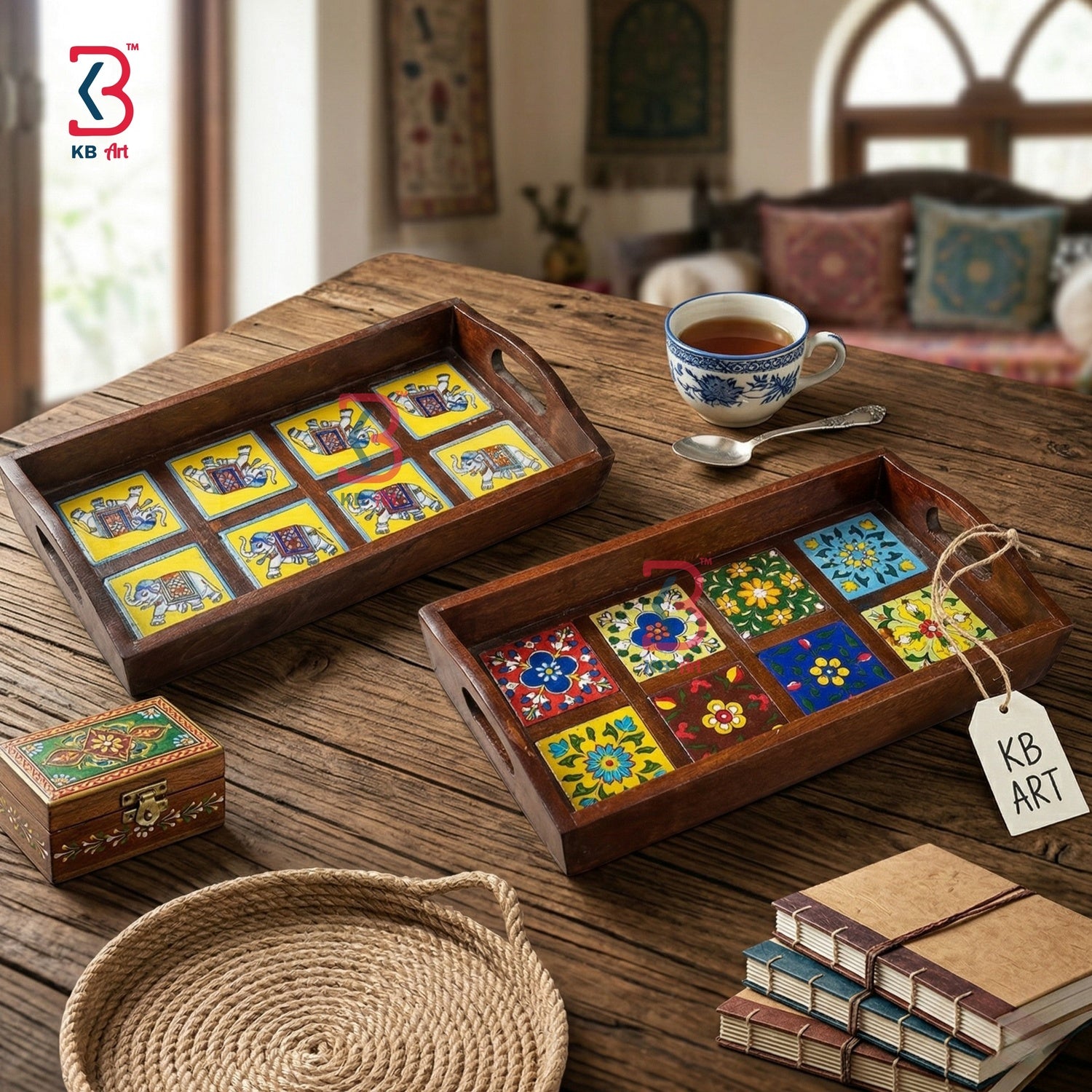Two decorative wooden serving trays with colorful mosaic tile patterns, displayed on a rustic wooden table alongside a teacup, books, a woven plate, and a small wooden box. The KB Art logo is visible in the top-left corner.