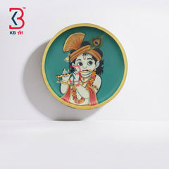 A round decorative wall plate featuring a colorful illustration of a child in traditional attire, mounted on a white wall. The plate has a teal background with a gold rim and a red KB art logo in the top-left corner.
