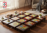 A set of low wooden coffee tables arranged in a room, each featuring a colorful mosaic tile top. The tables are styled with books, teacups, and a small potted plant on a wooden floor in a bright living space.