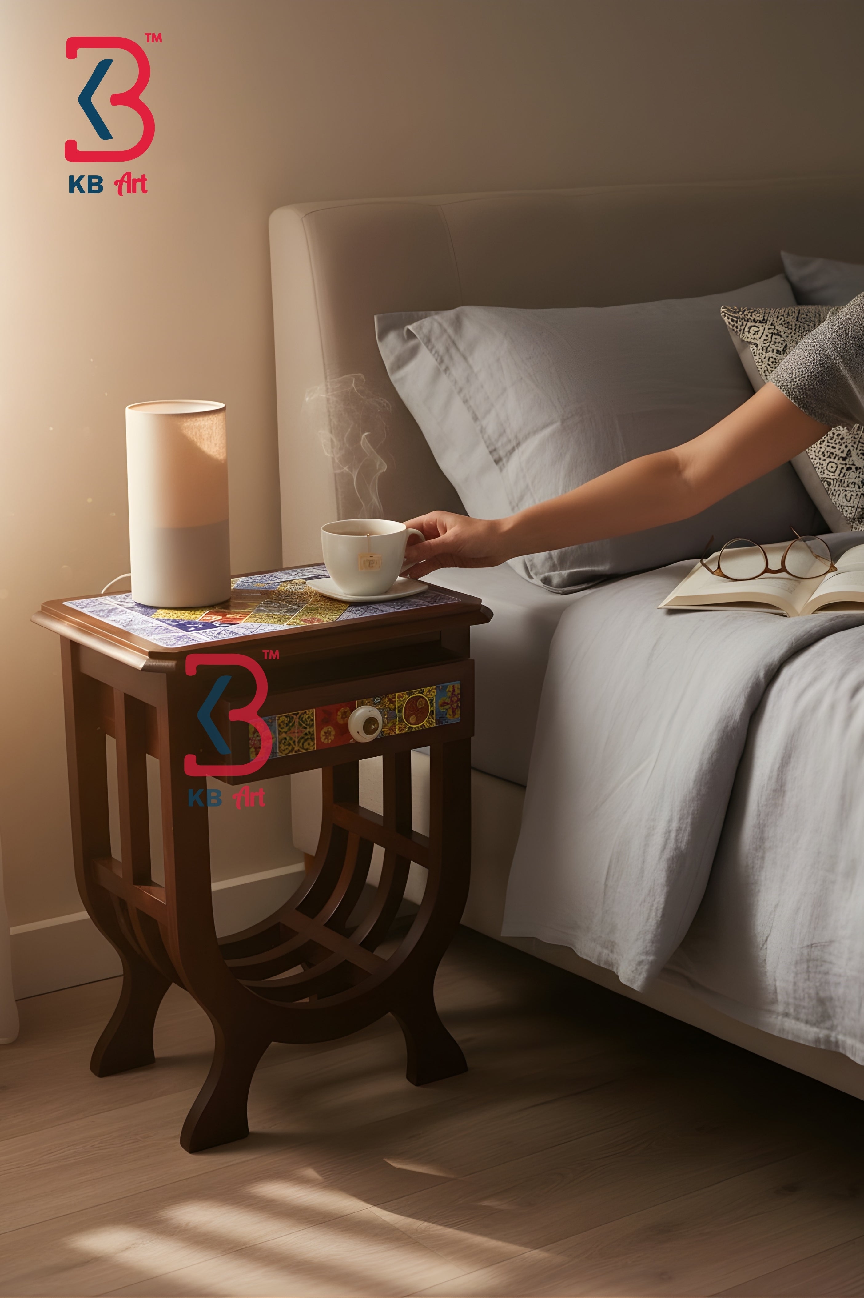 A dark brown wooden nightstand beside a bed, styled with a white cylindrical lamp and a steaming cup on a colorful mat. A person's arm reaches toward the cup.