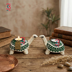 Two turtle-shaped candle holders with lit candles on a wooden surface, surrounded by books and plants. A styled lifestyle scene displaying the decorative hand-painted wooden tortoise stands glowing warmly on a festive living room table setup.