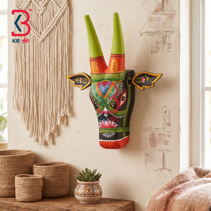 Black hand-painted wooden cow head wall hanging with green horns, lotus flower and tribal geometric design in a boho living room