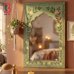 A decorative arched mirror with a painted green frame featuring floral and leaf motifs, shown hanging on a warm brown wall in a styled interior setting.