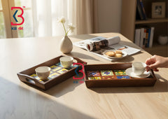 Two dark brown wooden serving trays with integrated handles, styled on a light wood table. One tray holds two small white teacups, and the other holds a white teacup and saucer while a hand is holding it.