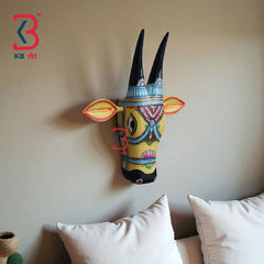 Ethnic carved wooden cow mask with ornamental detailing and lotus motifs on a rustic background.