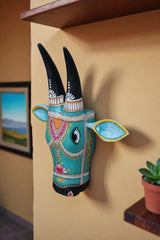 Decorative Indian wooden bull head with detailed blue and pink designs, mounted on a brick wall