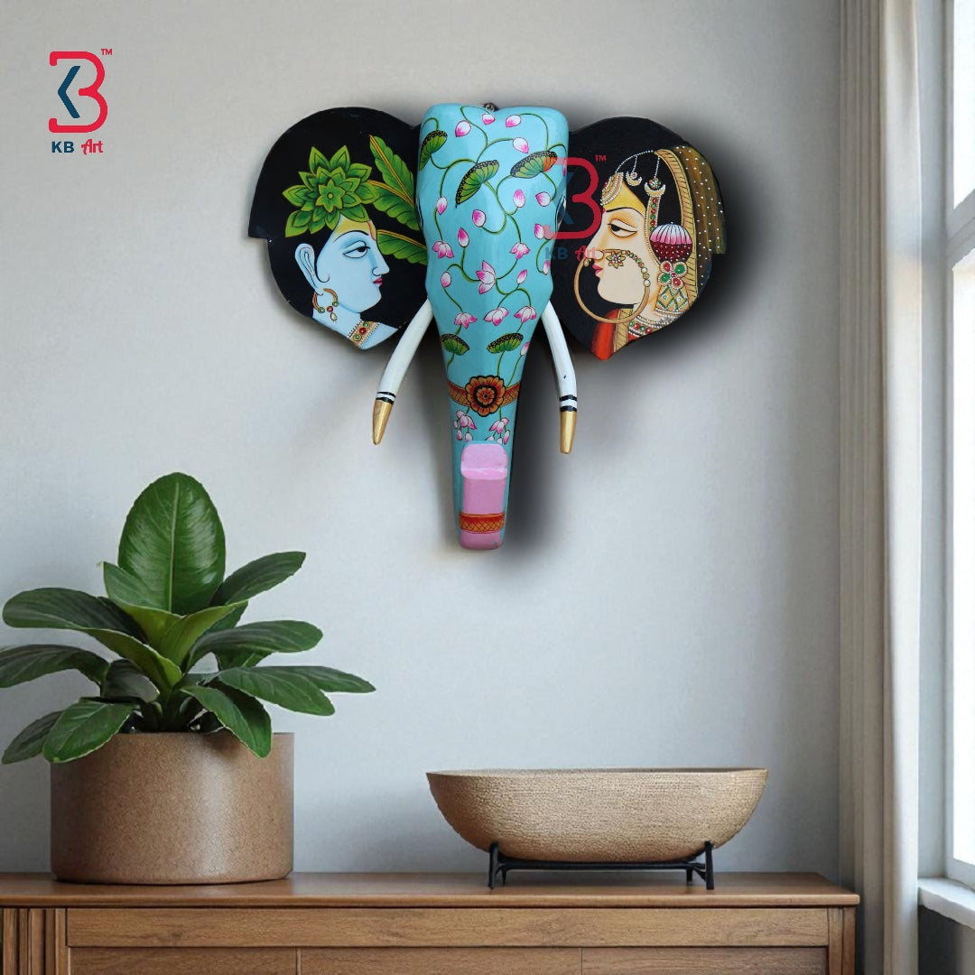 Ethnic wooden elephant mask with lotus floral motifs on a light blue background and gold-tipped tusks.