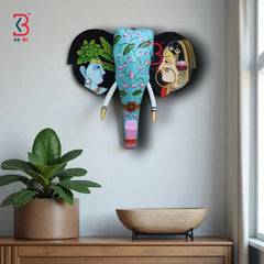 Ethnic wooden elephant mask with lotus floral motifs on a light blue background and gold-tipped tusks.