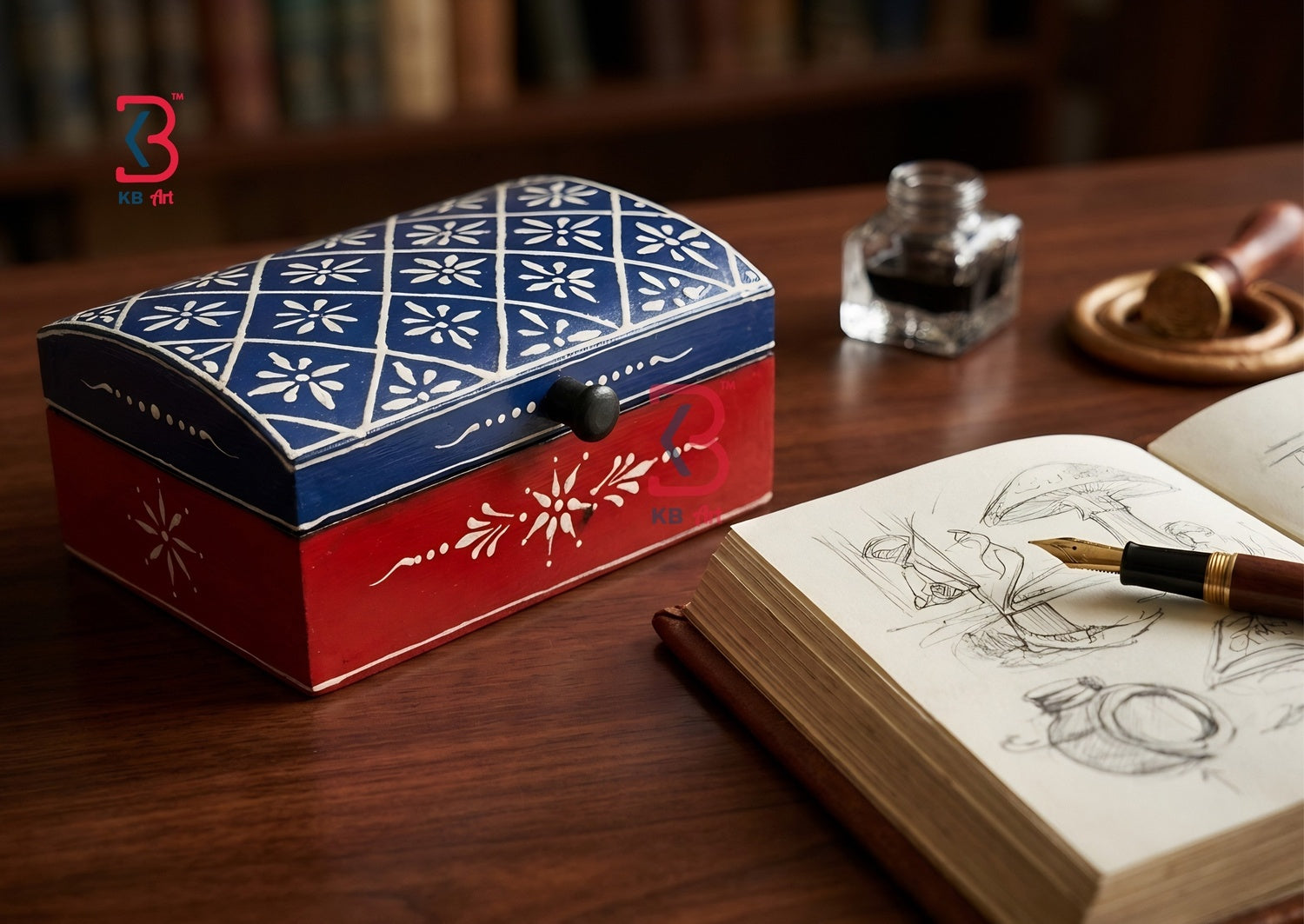 A decorative wooden keepsake box with a red base and a blue patterned lid, styled on a wooden desk next to an open sketchbook, fountain pen, and ink bottle.