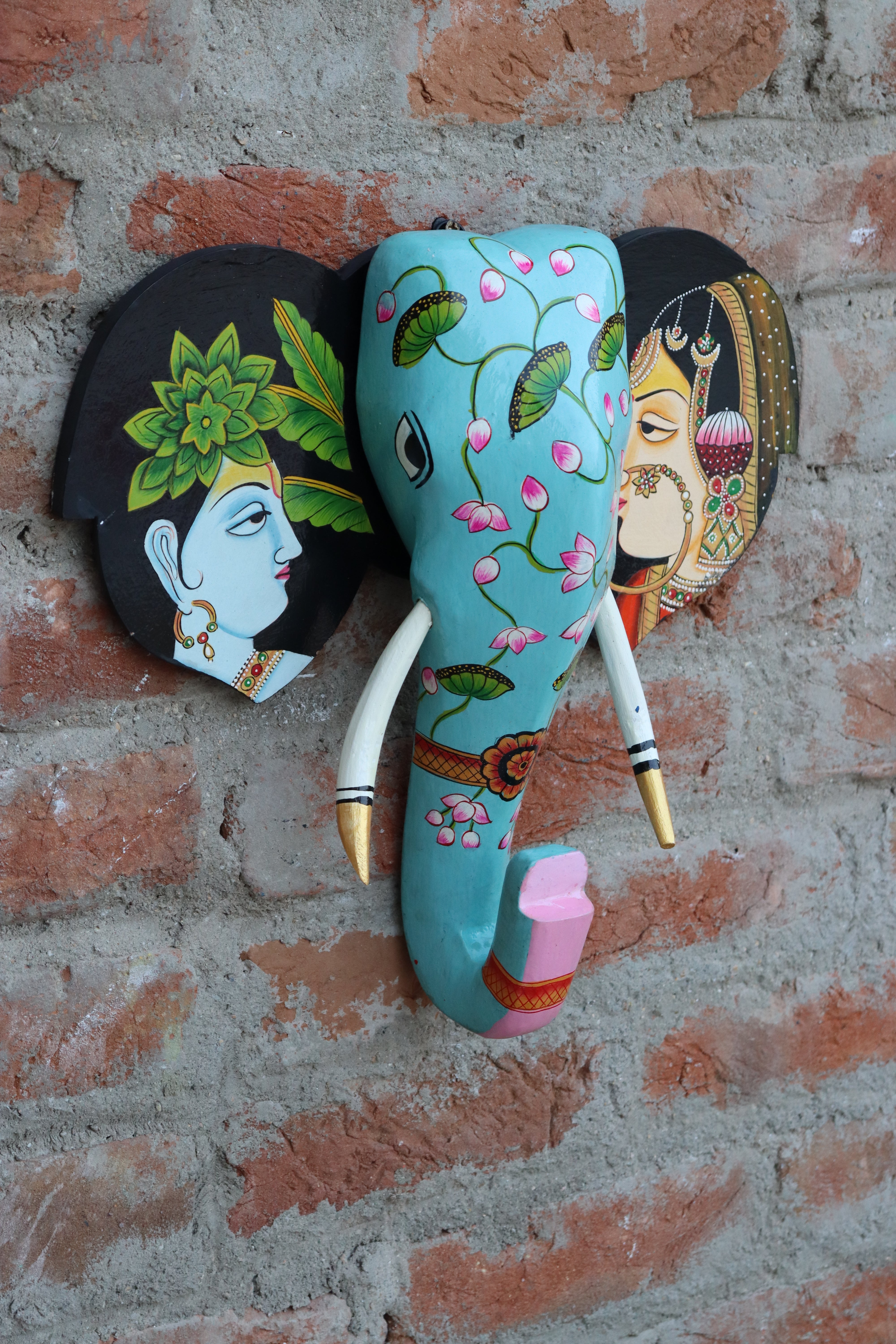 Cultural wooden elephant wall hanging with mythological figures and intricate patterns on a stone wall.