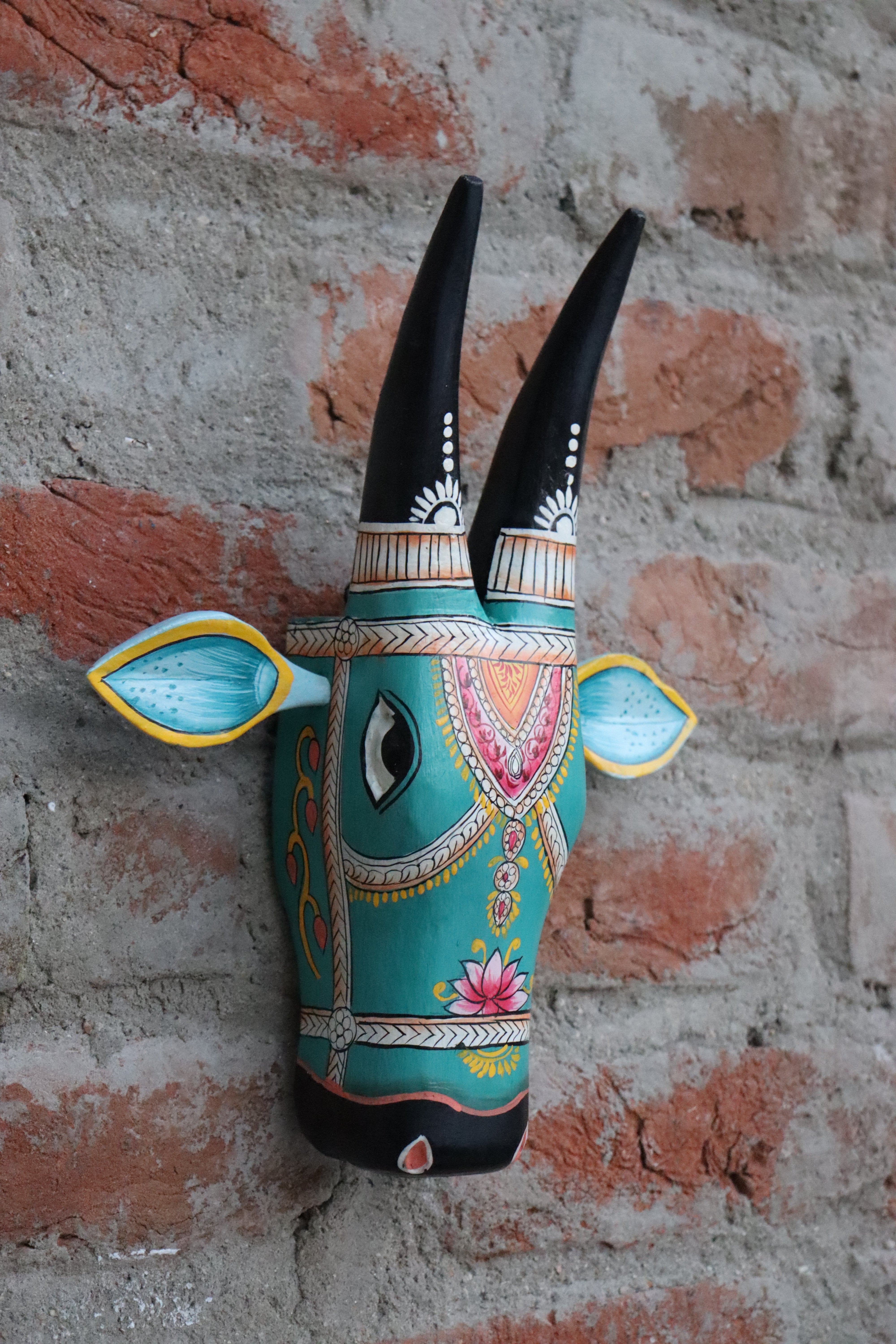 Colorful handmade wooden cow head for wall decoration, with intricate designs in pink, orange, and white.