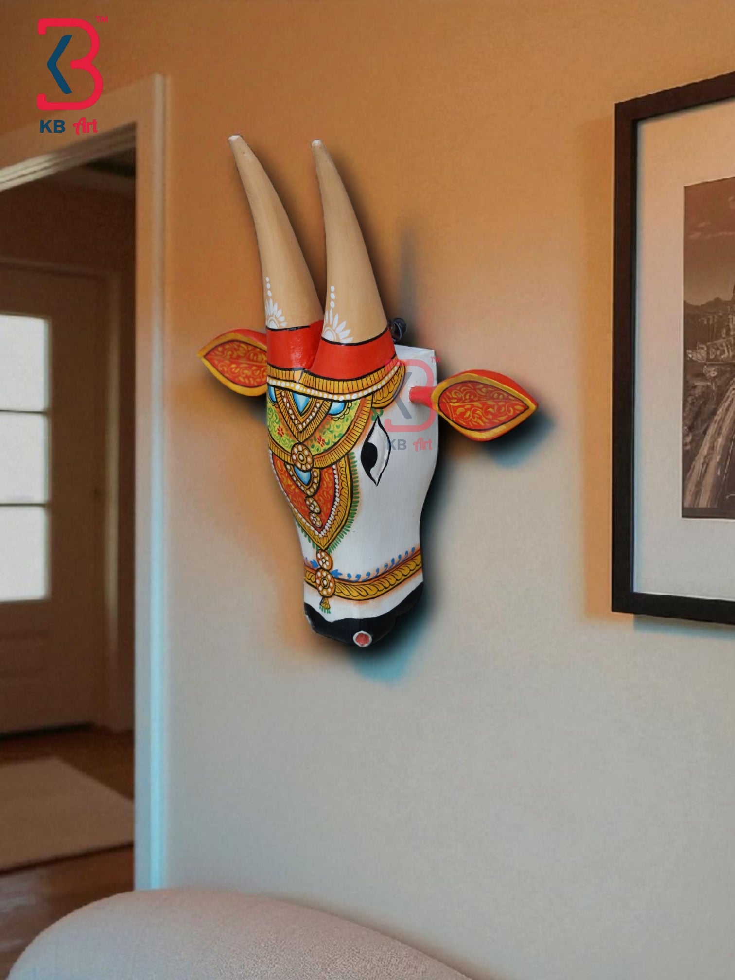 Decorative wooden cow bust with hand-painted details in gold, red, and turquoise, mounted on a brick wall