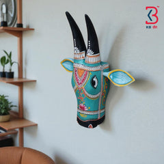 Artistic wooden bull head sculpture with black pointed horns and a turquoise body, showcasing traditional art.