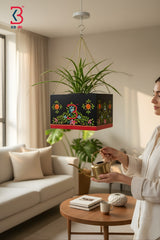 KB ART hand-painted black floral wooden hanging planter model featuring colorful vine motifs and a red bottom trim holding a green spider plant suspended by a golden chain.