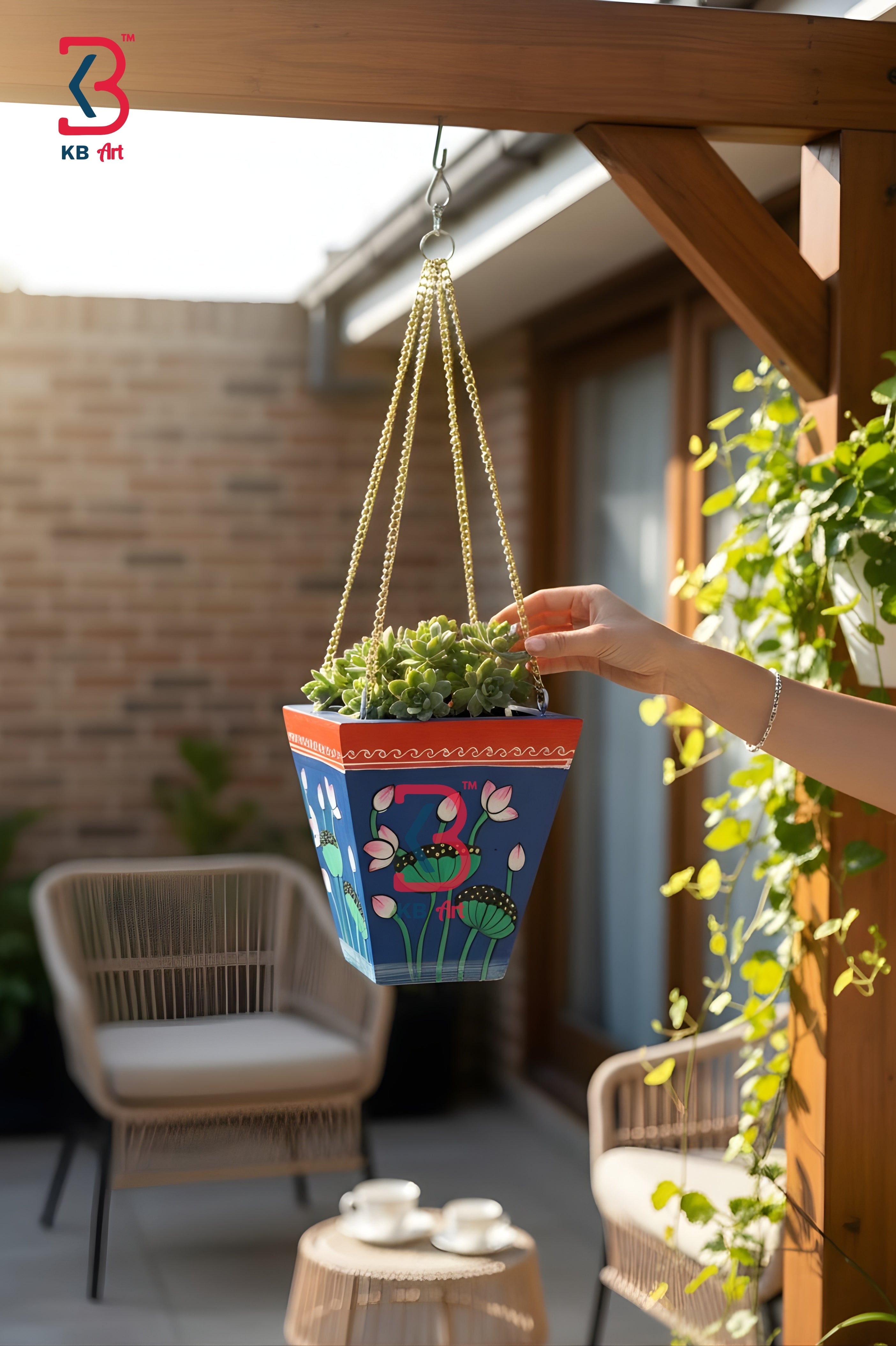 Person holding a colorful hanging plant pot with a blurred background of a patio area.