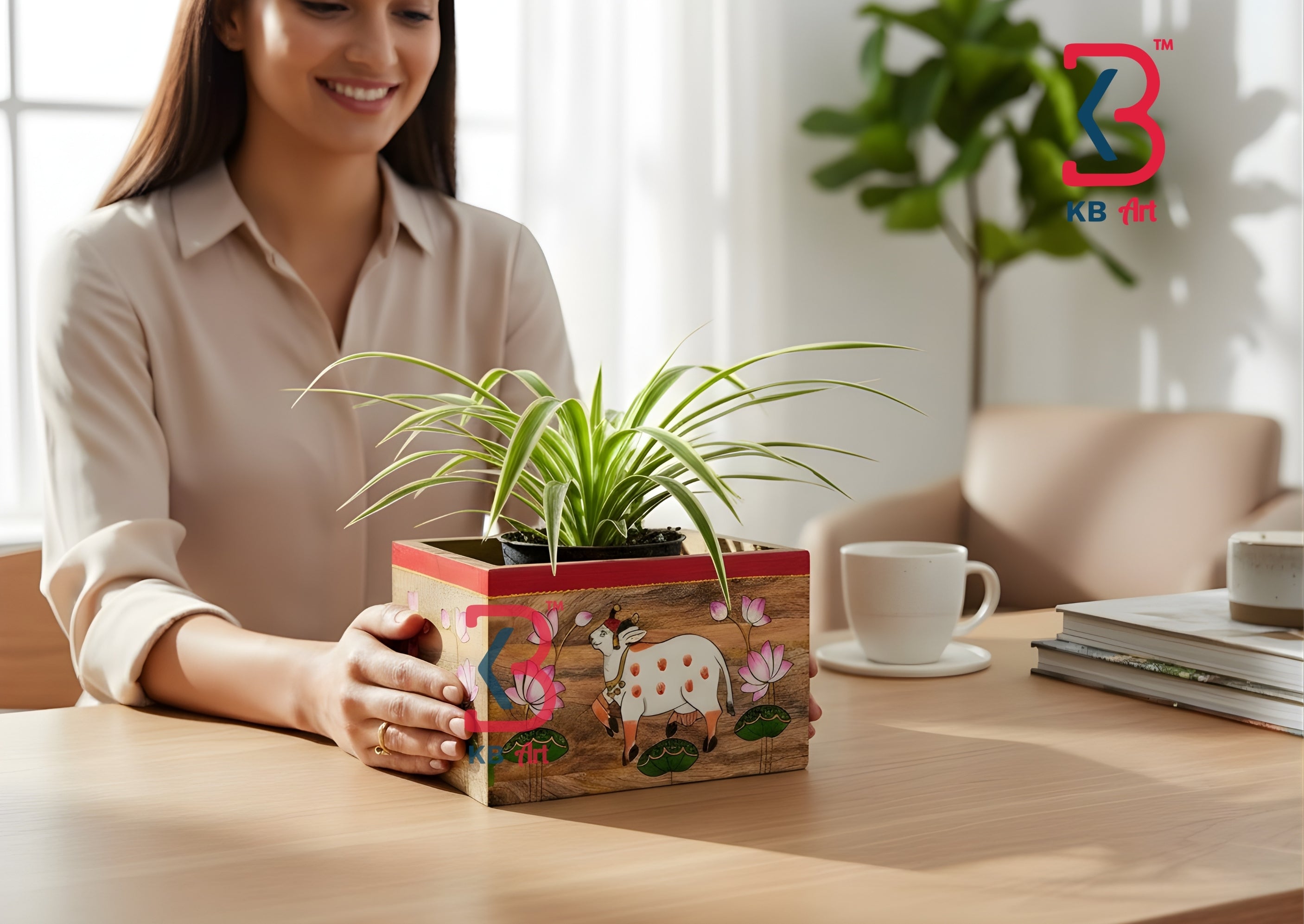 A woman  smiles while holding a small potted spider plant in a decorative wooden planter box with painted floral and animal motifs, set on a wooden table in a bright indoor setting.