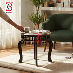 Person placing a cup on a wooden side table in a cozy living room with a green armchair and plants.
