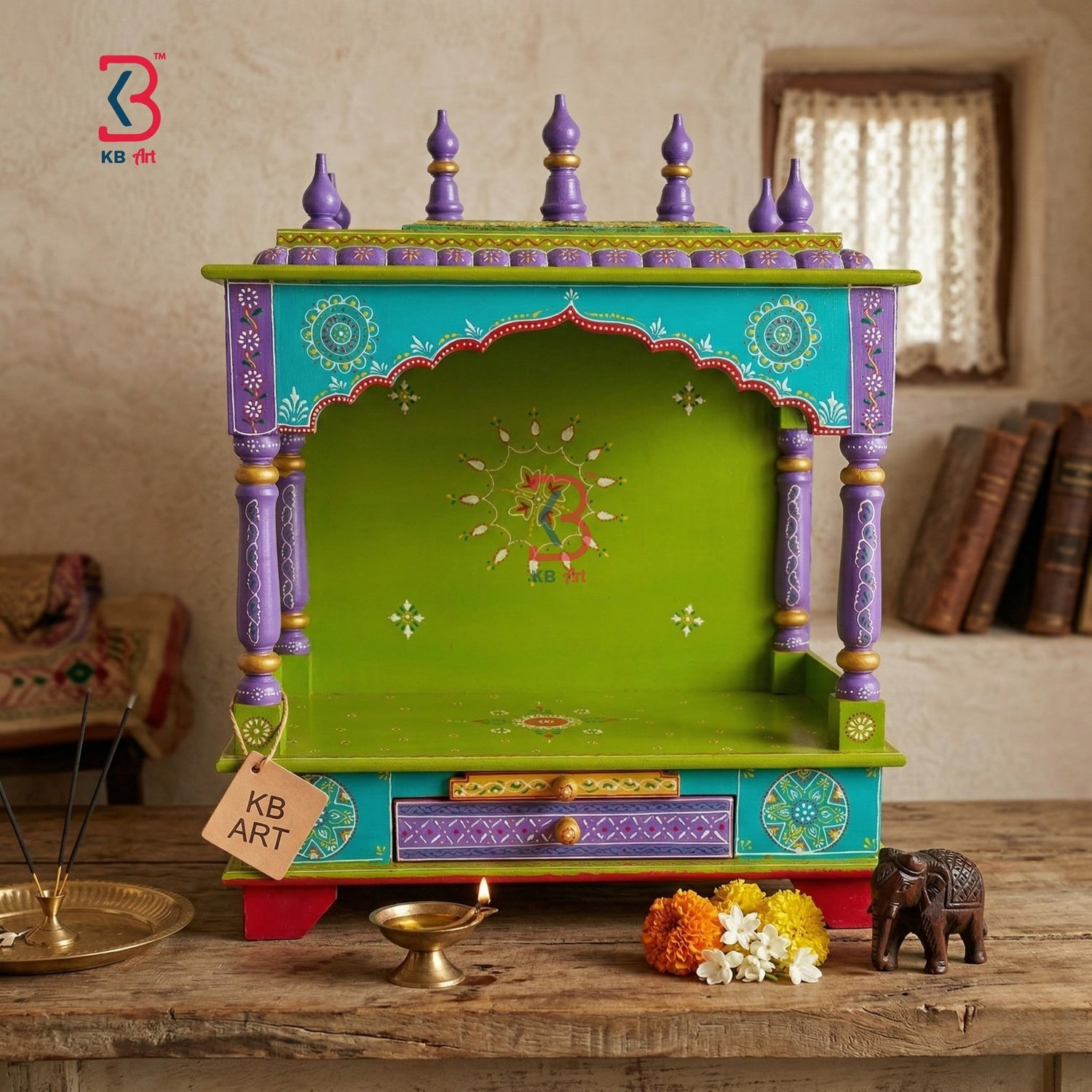 A hand-painted Indian wooden Shiva mandarin altar (dehe) on a rustic wooden table, decorated with vibrant green, turquoise, purple, and gold colors, with a small brass lamp and flowers in front.