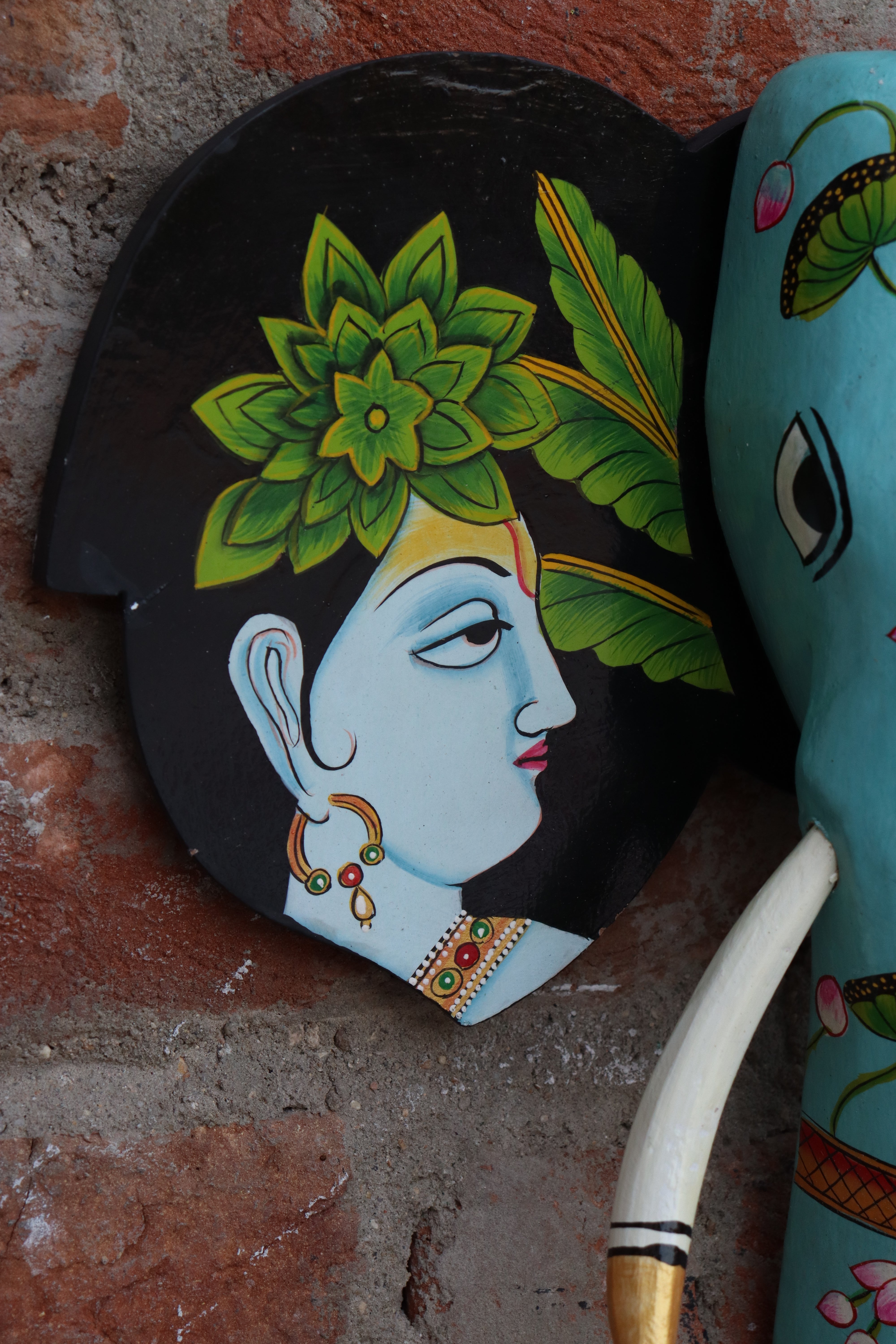 Ornate wooden elephant wall art with a light blue body, pink flowers, and black ears with detailed figures.