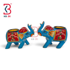A pair of hand-painted blue elephant candle holders with red, yellow, and orange decorative patterns, shown on a white background with a KB Art logo.