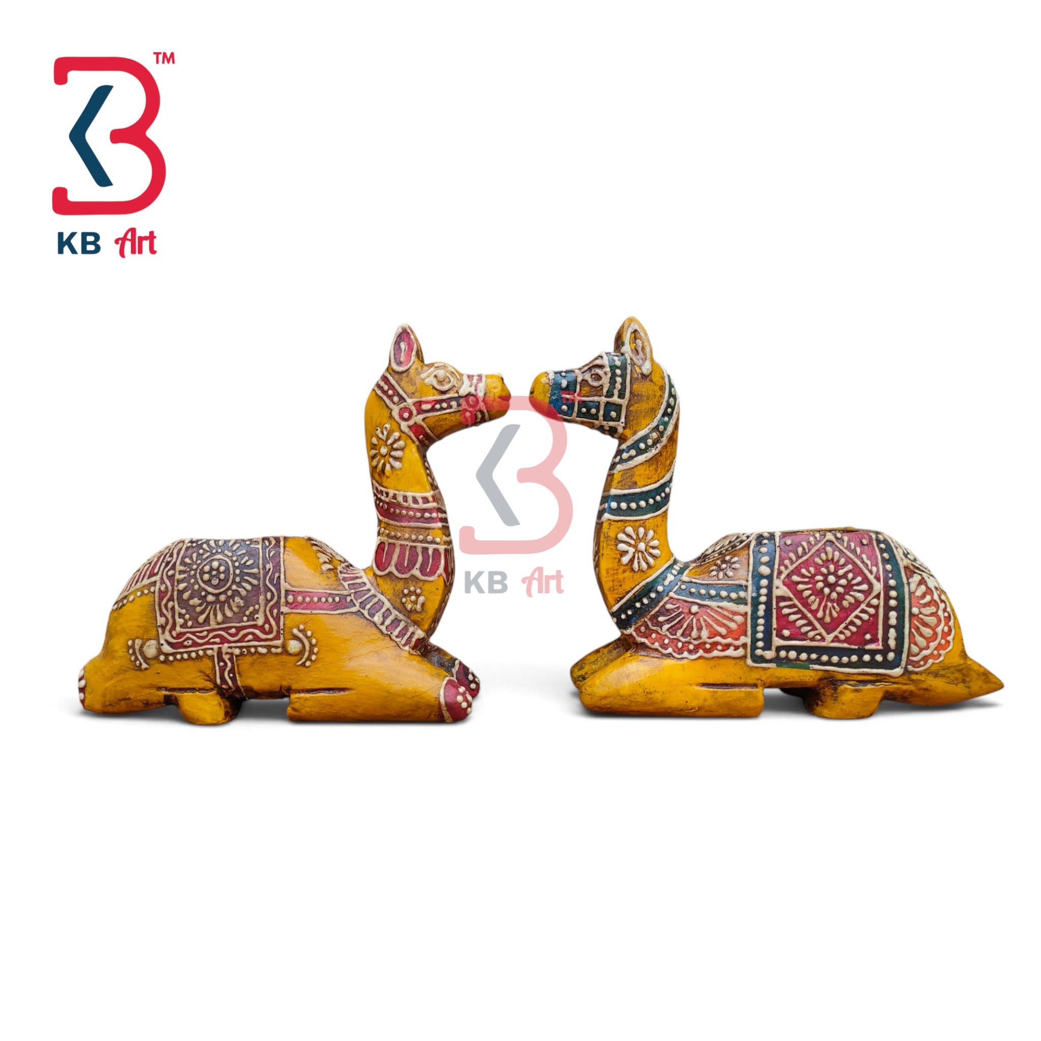 Two hand-painted wooden camel figurines facing each other, decorated with intricate red, black, and white folk art patterns on a yellow-brown base, shown on a white background with a KB Art logo.