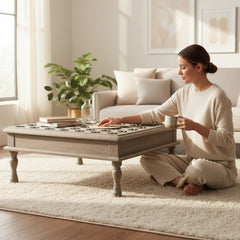 A woman in a beige lounge set sits cross-legged on a white shag rug beside a light gray wooden coffee table in a bright, modern living room.