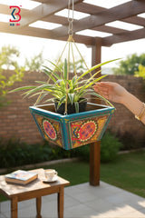 Hanging planter with colorful floral design held by a hand outdoors.