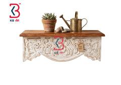 KB ART hand-carved ornate wooden wall shelf with a natural finish top and distressed white-washed floral base holding a succulent planter and a brass watering can.