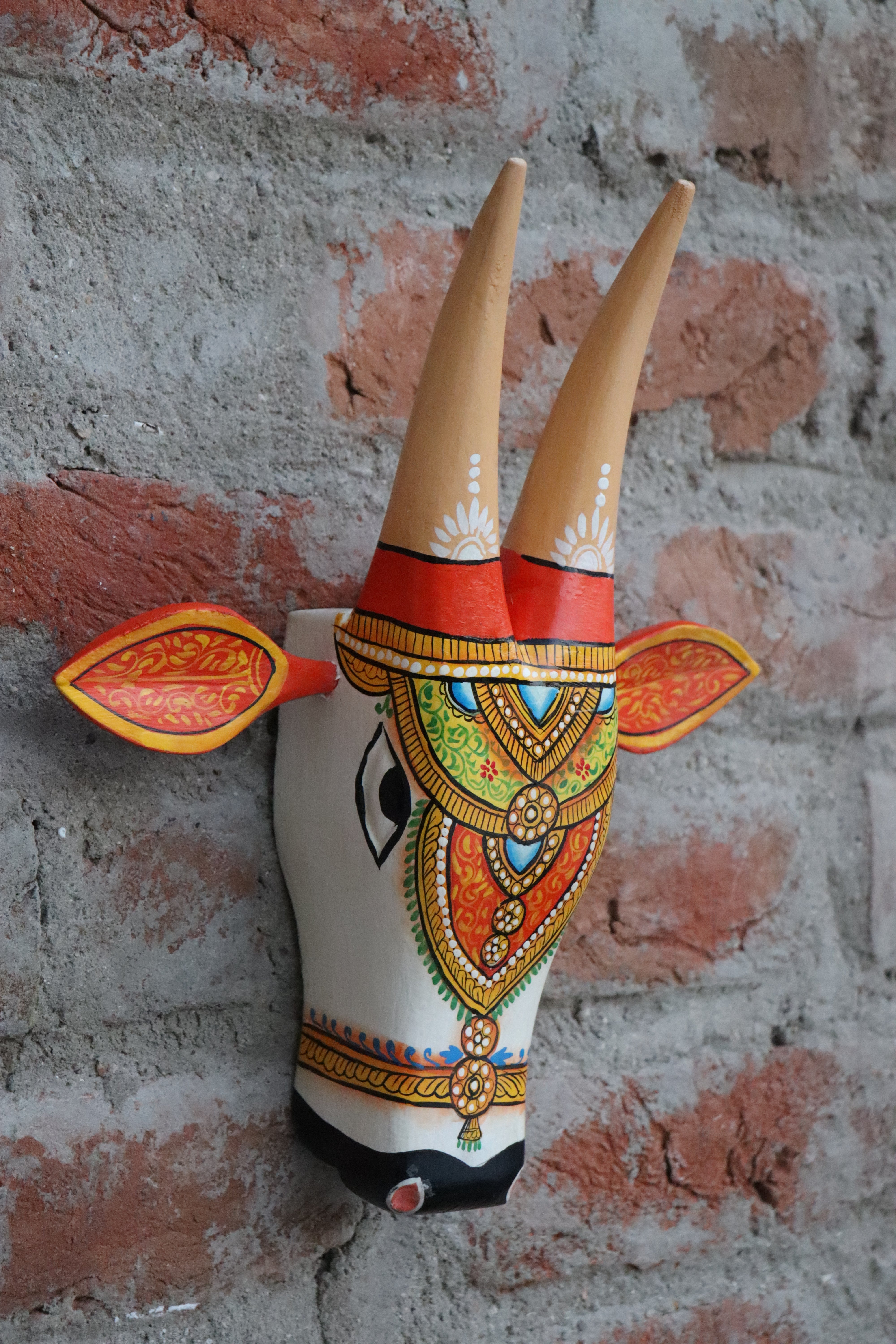 Ornate wooden cow wall hanging, painted with traditional motifs and bright colors.