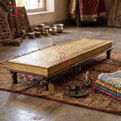 Decorative wooden bench with gold leaf finish on a textured rug, surrounded by decorative items.