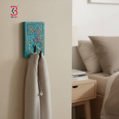 A turquoise blue carved wooden wall hook with a hanging scarf and necklace, shown in a softly lit bedroom setting.