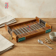 A rectangular wooden serving tray with decorative inlay details, shown on a wooden tabletop with folded napkins, a small bowl, and a spoon nearby. A KB retail logo appears in the top left corner.