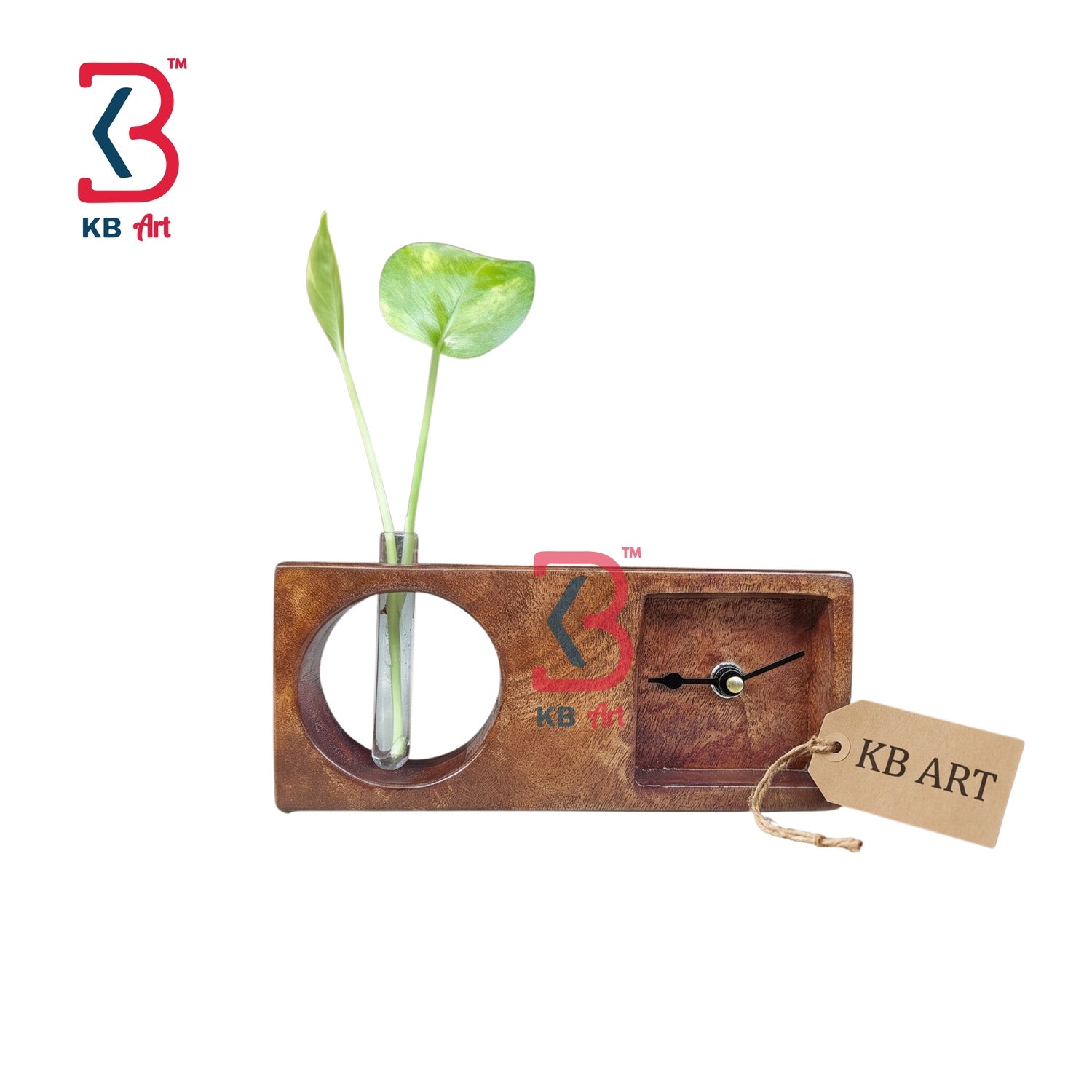 A rectangular wooden wall clock with a circular cutout holding a green plant stem and a small inset clock face. The wood has a warm brown finish, and a small paper tag reading KB ART hangs from the clock.
