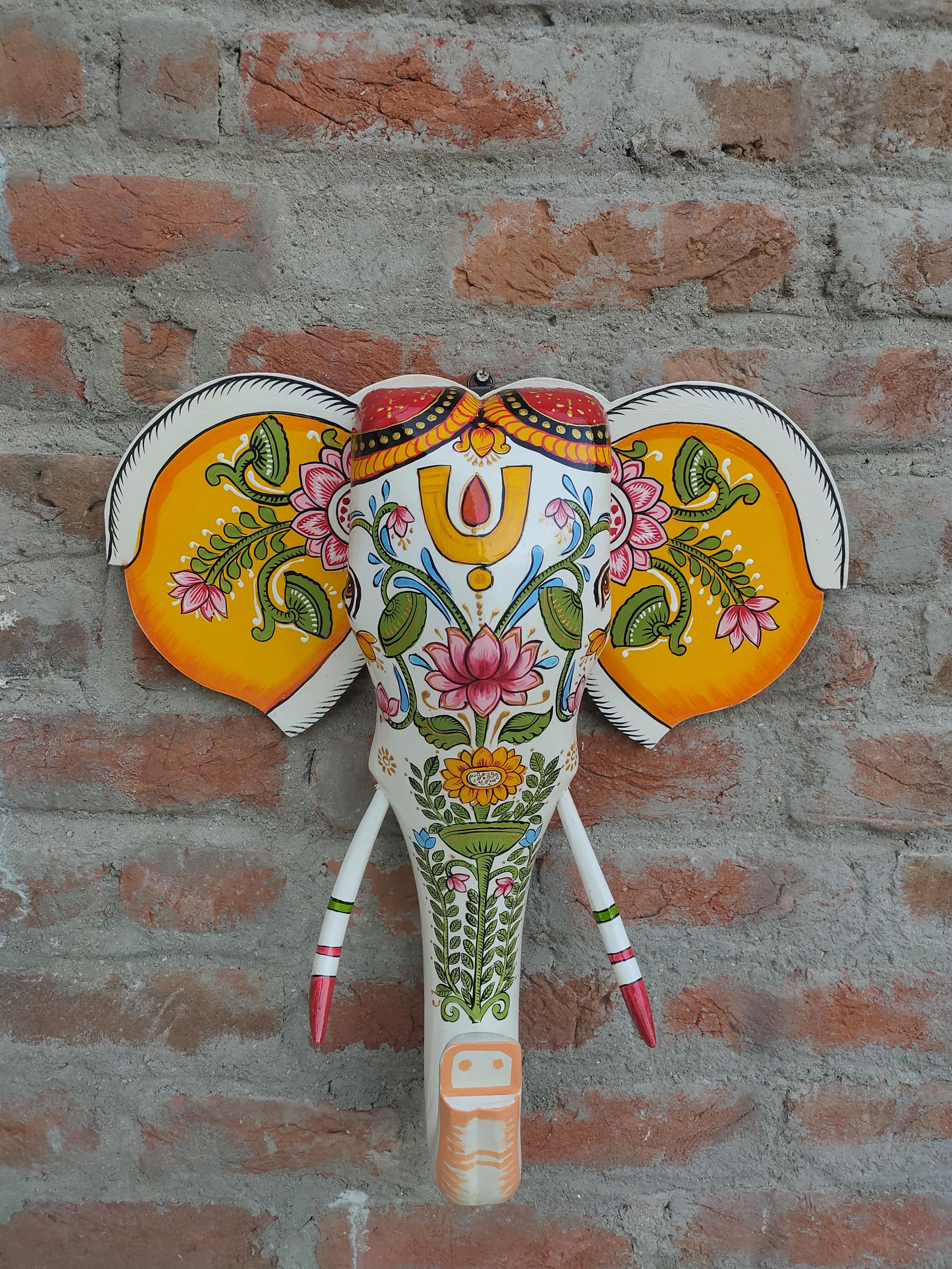 Hand-painted wooden elephant head wall decor with intricate floral designs on a brick background.