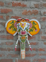 Hand-painted wooden elephant head wall decor with intricate floral designs on a brick background.