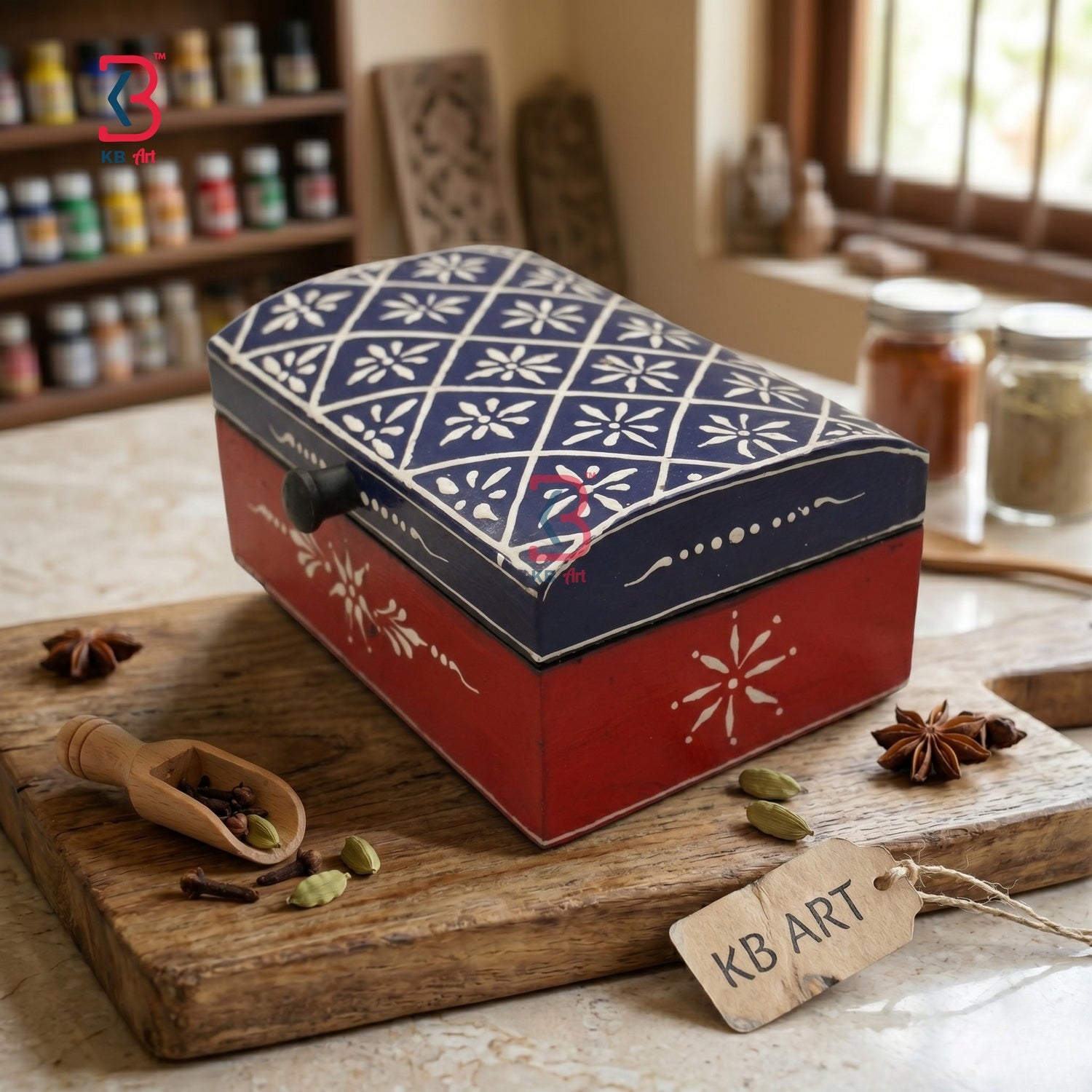 A decorative rectangular spice box with a red base and a navy blue lid featuring white snowflake patterns, displayed on a wooden cutting board with spices in a kitchen setting.