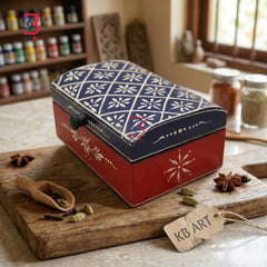 A decorative rectangular spice box with a red base and a navy blue lid featuring white snowflake patterns, displayed on a wooden cutting board with spices in a kitchen setting.