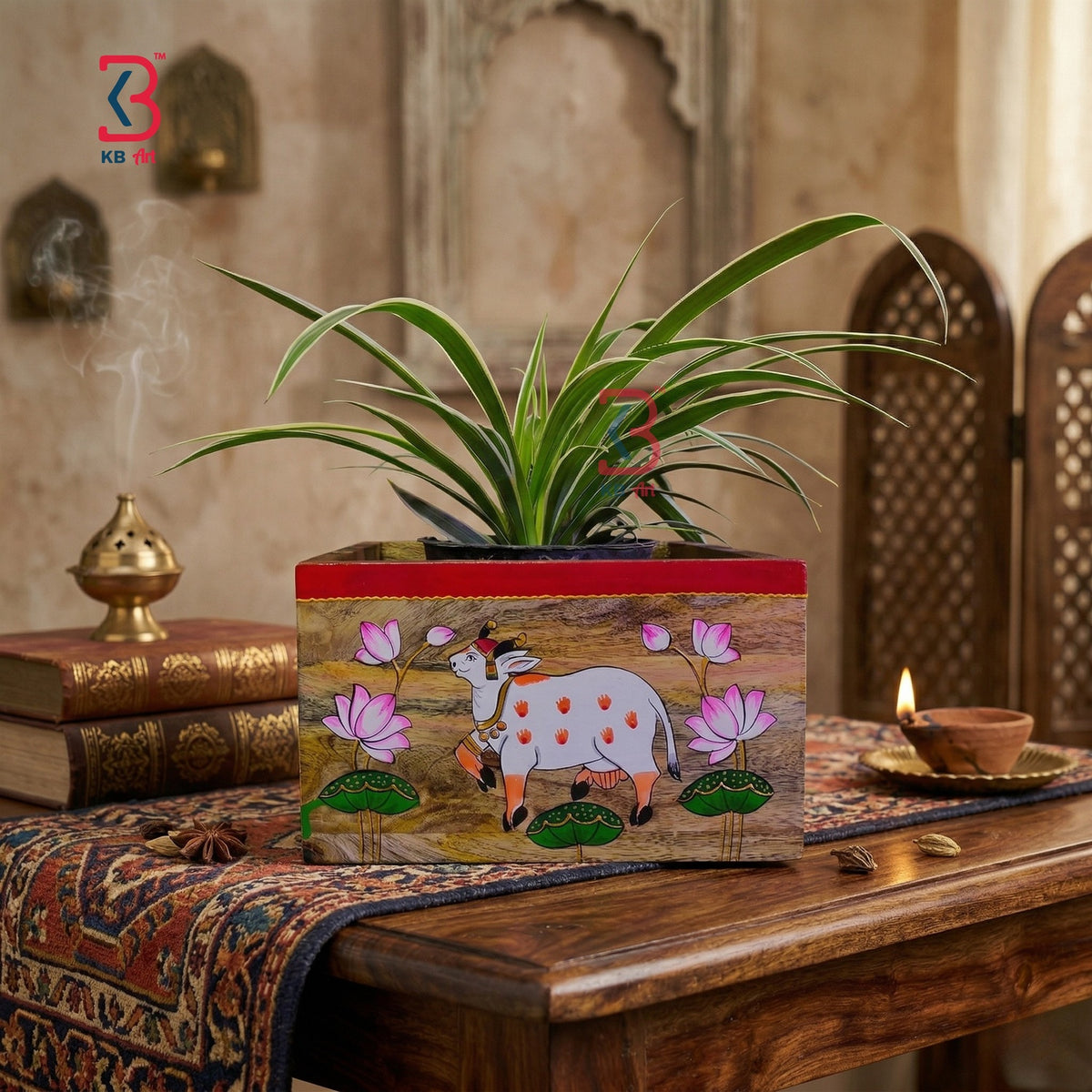 A rectangular wooden planter box with a hand-painted cow and lotus design, placed on a wooden table in a styled room setting with a potted plant on top.