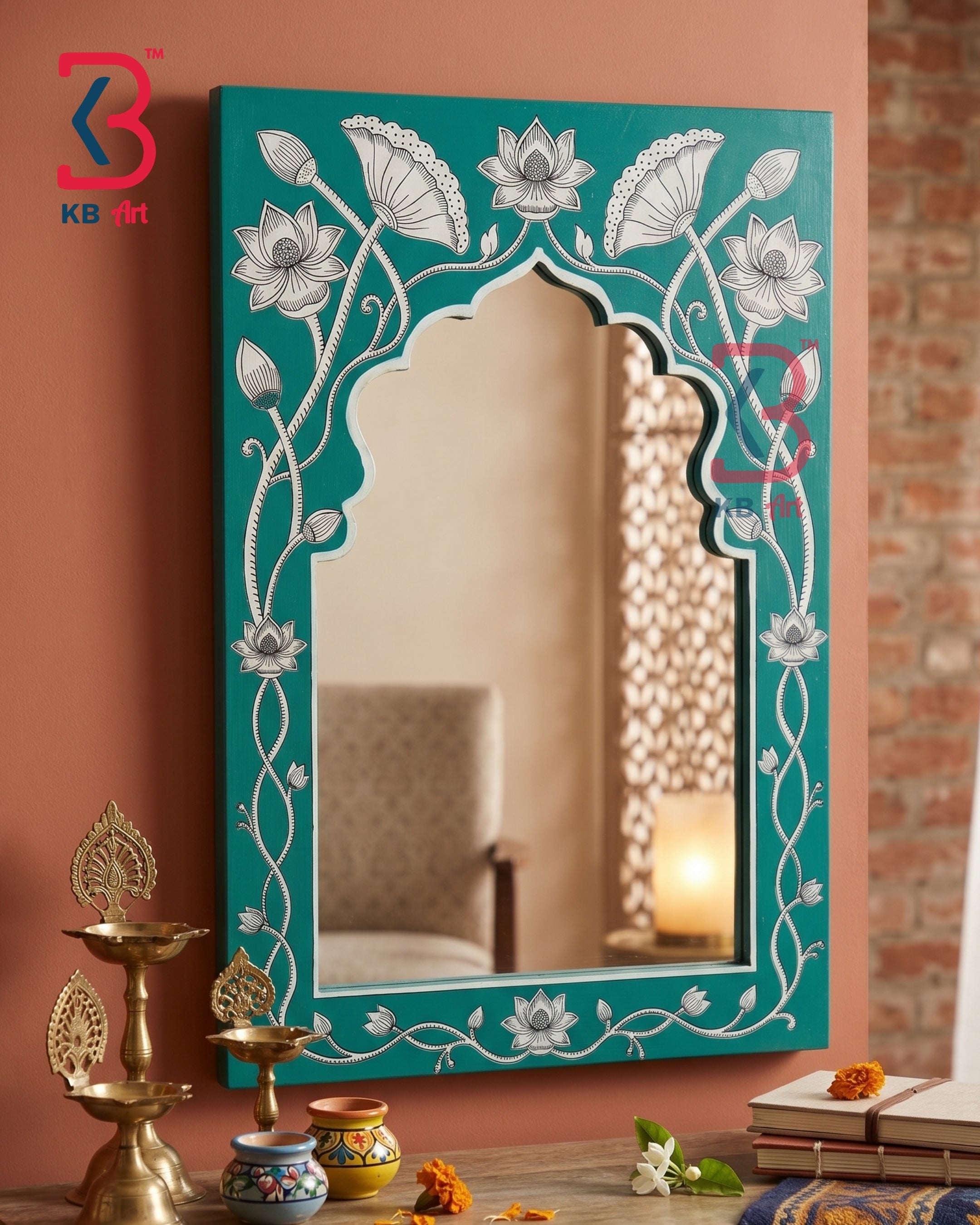 A decorative arched wall mirror with a turquoise frame featuring hand-painted white lotus flowers and vine motifs, styled in a warm, rustic room setting with brass oil lamps and books.