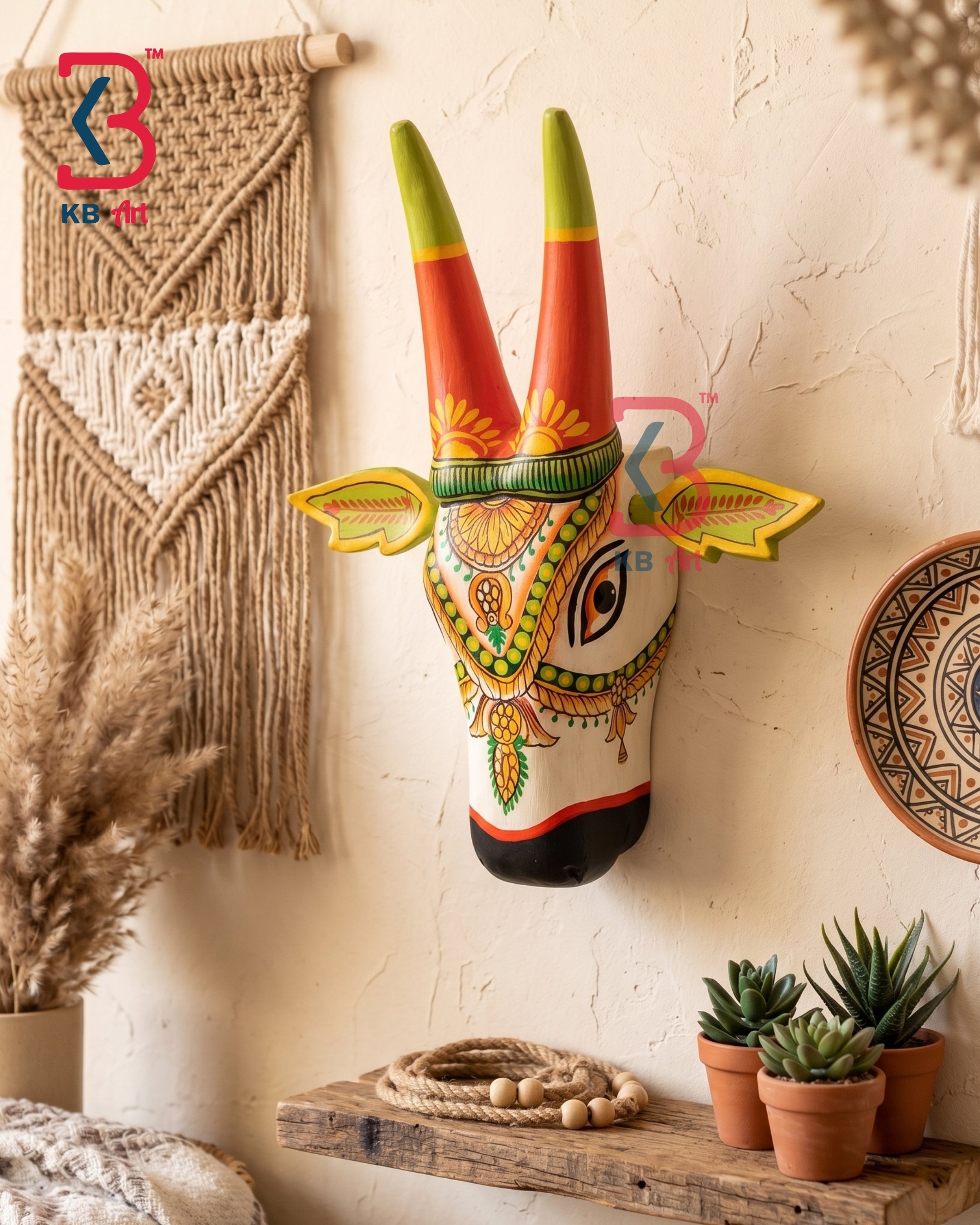 A hand-painted wooden Aves (deer) wall hanging mounted on a textured beige plaster wall, styled with boho decor including a macrame wall hanging, dried pampas grass, a wooden shelf with succulents, and a woven plate.
